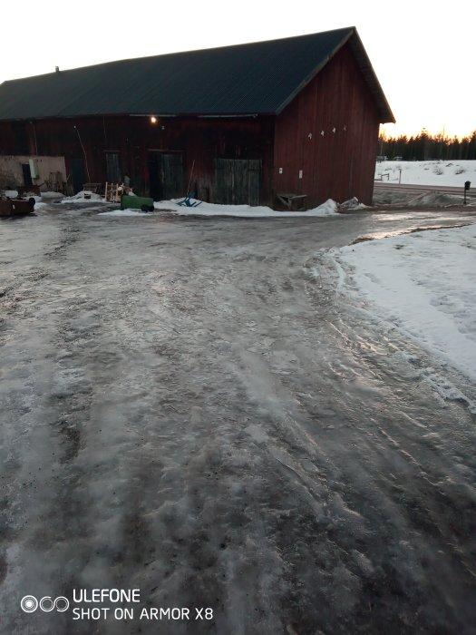 Isig gångväg leder fram till en röd ladugård i ett vinterlandskap, vilket föreslår en halkrisk.