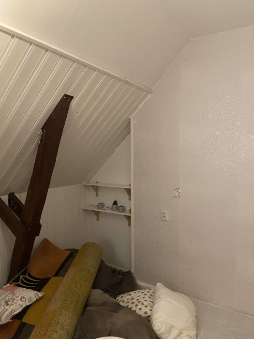Inredningsbild med synliga takstolar och lutande tak, möblerat rum med soffa och kuddar.