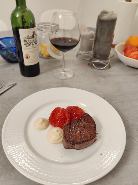 Stekt oxfilé med gratinerade tomater och ankleverskum, serverad på tallrik bredvid ett glas rödvin.