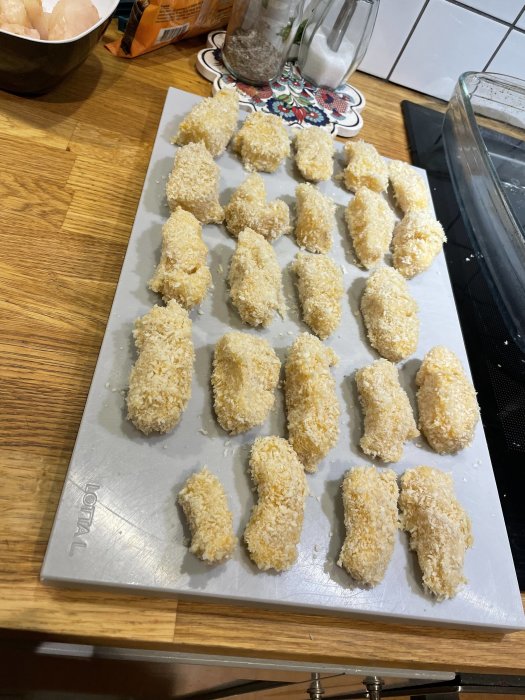 Råa fiskbitar panerade i ströbröd på en plåt redo för tillagning av fish tacos.