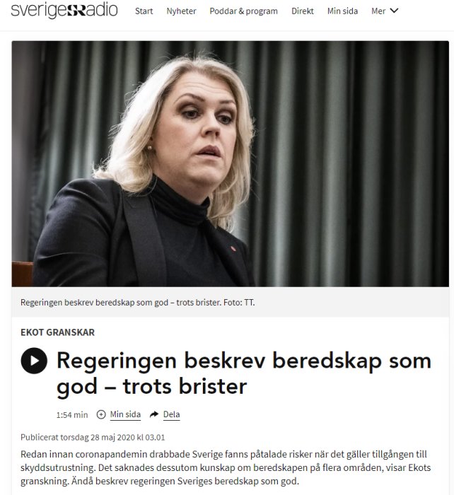 Allvarsam kvinna talar inför mikrofoner, sannolikt i politiskt sammanhang.
