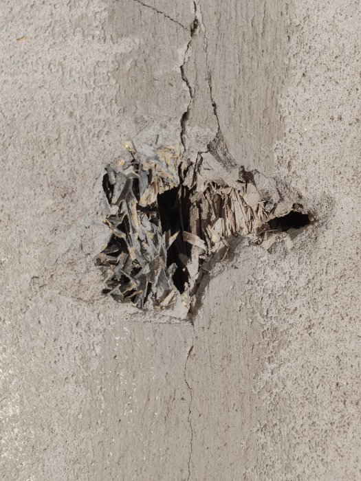 Skadad yttervägg med ett hål som exponerar poröst material liknande spånskiva bakom putsen i ett hus från 1964.