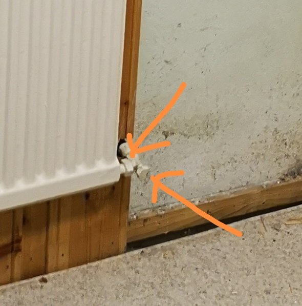 Värmeelement med läckande vatten vid anslutning mot en vägg, markerat med orange pilar.
