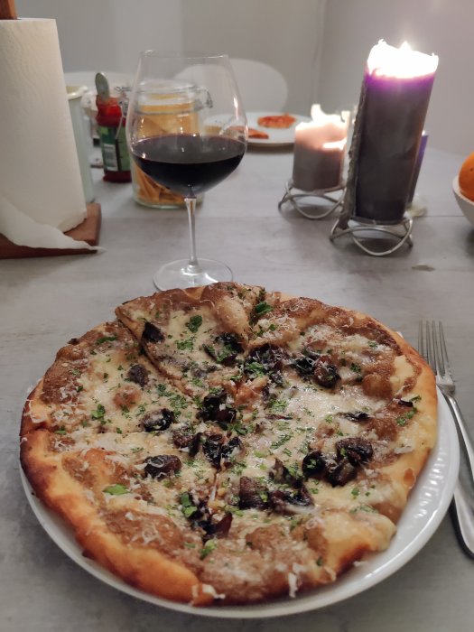 En tryffelpizza på tallrik med ett glas rödvin och brinnande ljus i bakgrunden.
