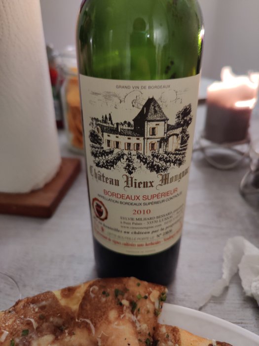 Flaska Bordeaux-vin från 2010 står på ett bord med suddig bakgrund av mat och ljus.