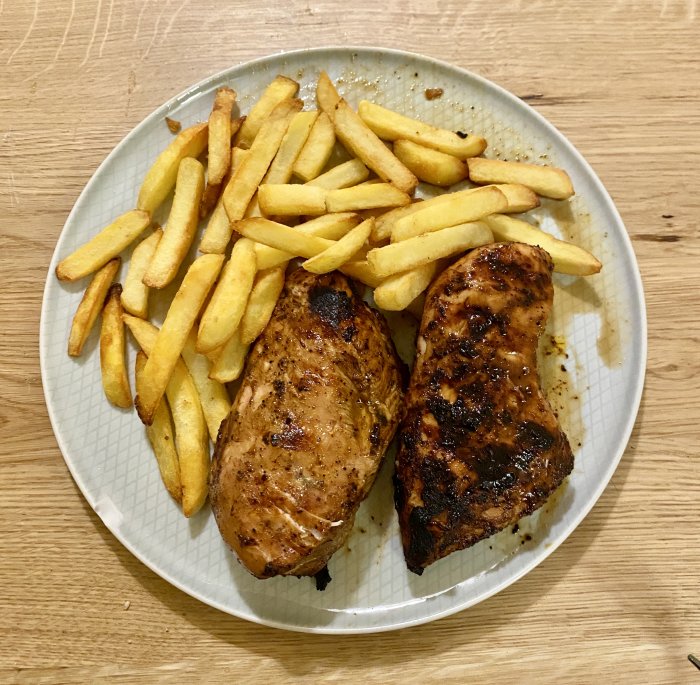 Två grillade kycklingfiléer med pommes frites på en tallrik.
