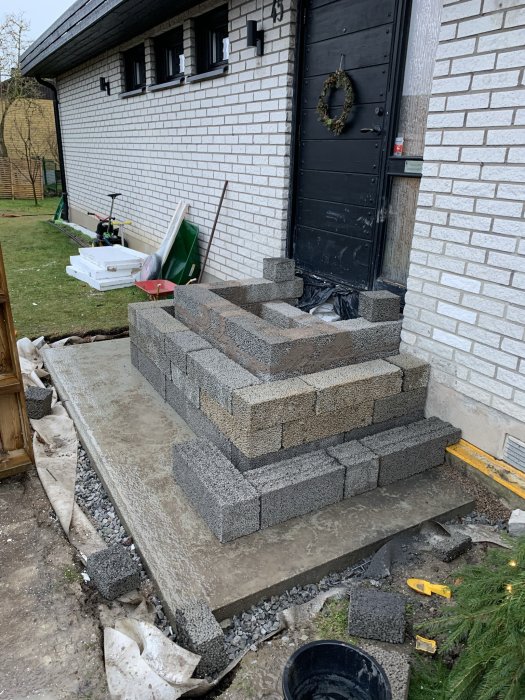 Betongblockstrappe under konstruktion framför en ytterdörr, uppbyggd med överhängande lager.