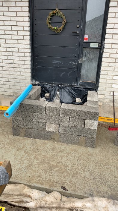 Betongblock konstruerade stegvis under en dörr med dräneringslist och plastskydd.