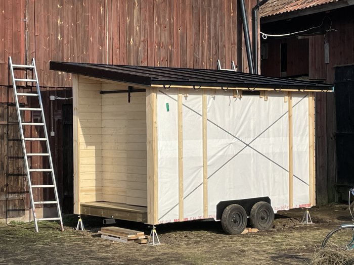 Hemsnickrad bastu på en balkärra under konstruktion med synlig träfiberisolering och obehandlad ytterpanel.