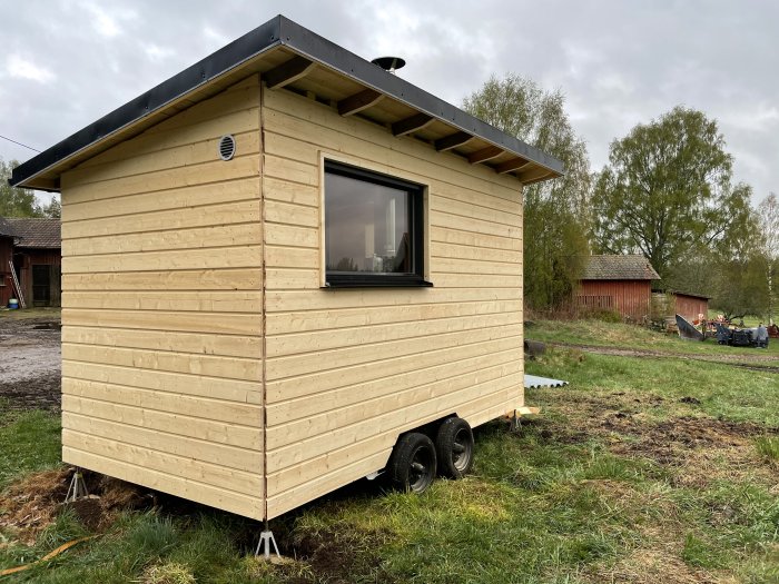 Nybyggd bastu på en gammal balkärra med obehandlad träpanel och tak, belägen på en äng.