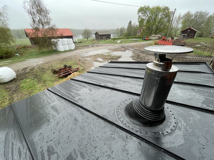 Vy från ett bastutak med skorsten över en regnig landsbygdsgård.