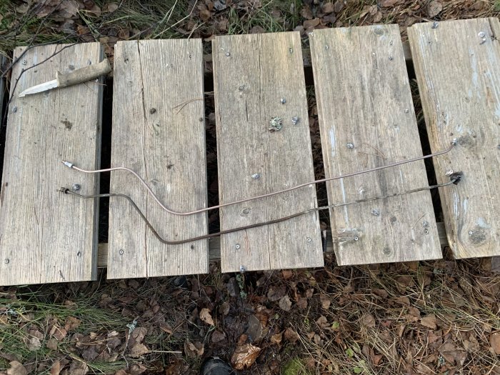 Metallbromsrör och nipplar placerade på träplankor på marken, verktyg synligt vid sidan.