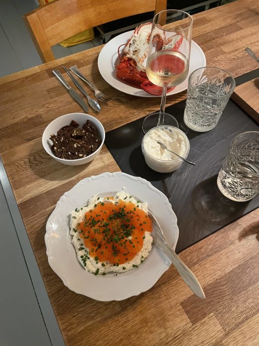 Måltid med skaldjur, ostbricka, rom på färskost, vin och vatten på träbord.
