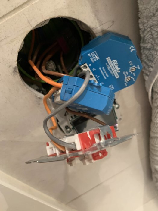 Öppen elinstallation med blå universal tryckdimmer och elledningar bakom en väggknapp.