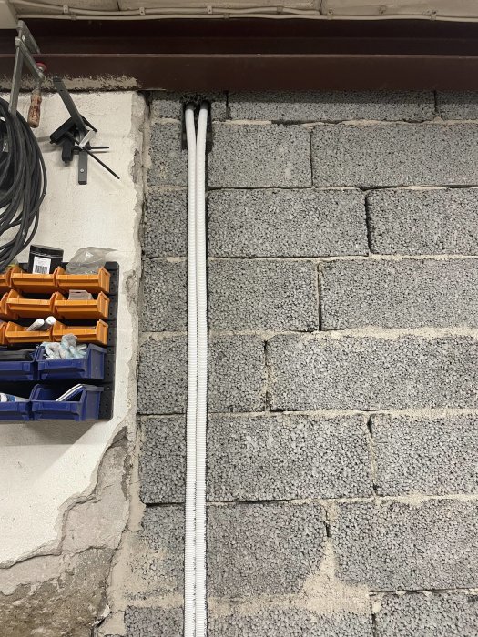 Rör installerade längs en betongvägg med en verktygslåda och kabelvinda i förgrunden.