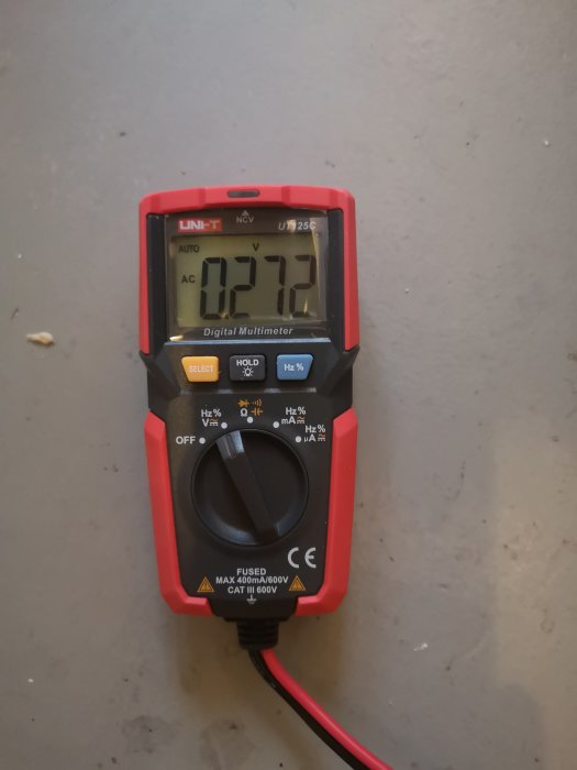 Digital multimeter som visar en mätning på 127.2 volt på en grå yta.