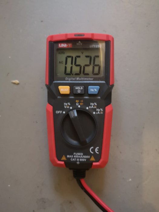 Digital multimeter visar 502.6 volt på skärmen, ligger på en grå yta.