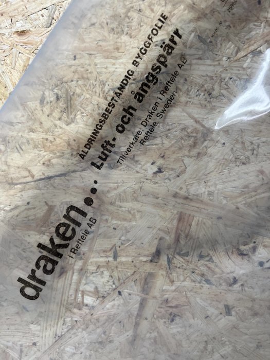 Transparent byggfolie med texten "draken" över OSB-skiva (oriented strand board).