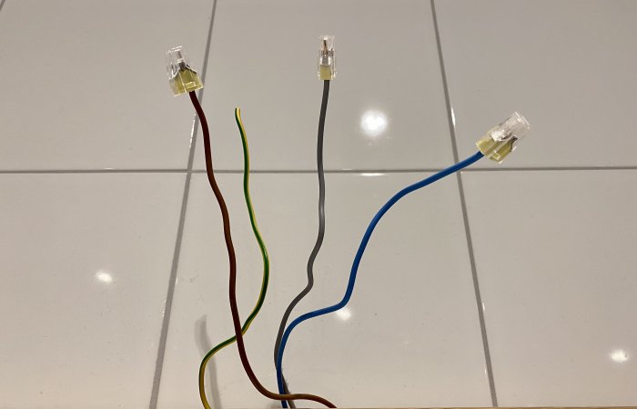Elektriska kablar med olika färger samt anslutningsklämmor på en vit kakelbakgrund.