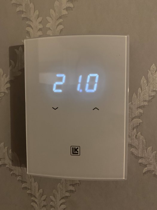 Digital termostat på vägg med display visande 21.0 grader Celsius.