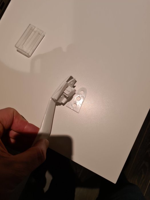 Hand håller en målarfärgsskrapa över en vit yta med ett skyddsplasthölje bredvid.