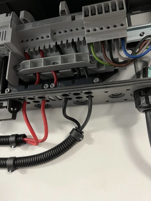 Elcentral monterad på vägg med rör och kablar anslutna till säkringsmoduler.