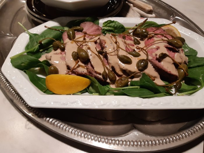 Vitello tonnato på en bädd av spenat med kapris och citronskiva på ett silverfat.
