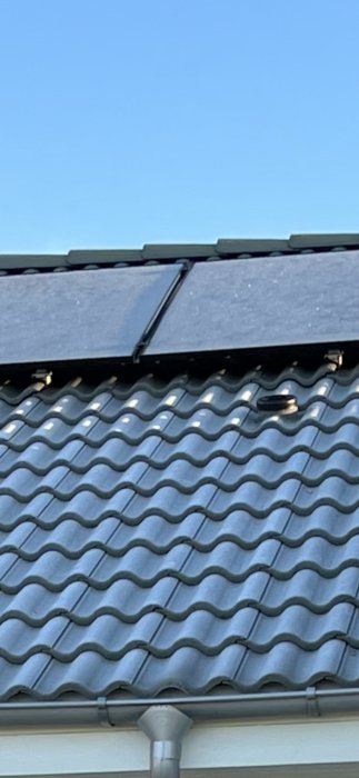 Takpannor med monterade solpaneler och takkrokar på ett tak, visande installationen.