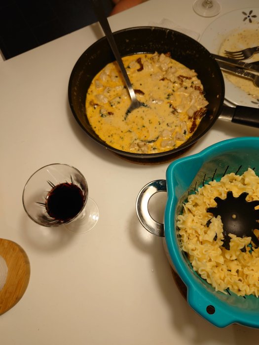 Kycklingrätt med gräddig parmesansås och basilika i stekpannan bredvid pasta och glas med rödvin.