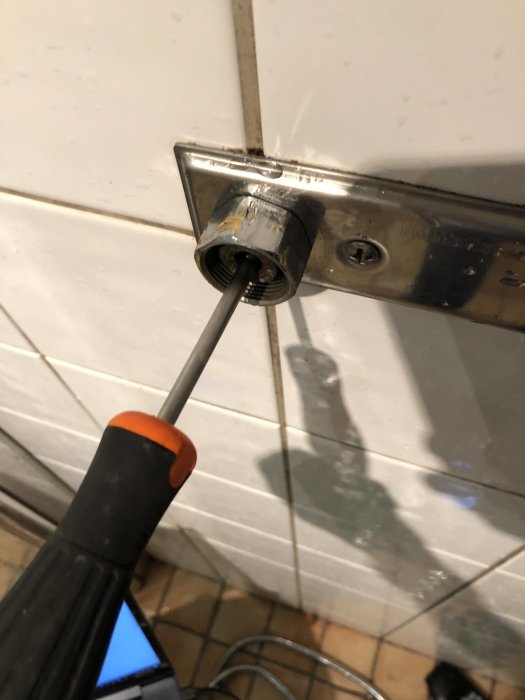 Skruvmejsel insatt i öppet vattenrör för inspektion i vägg med kakel.