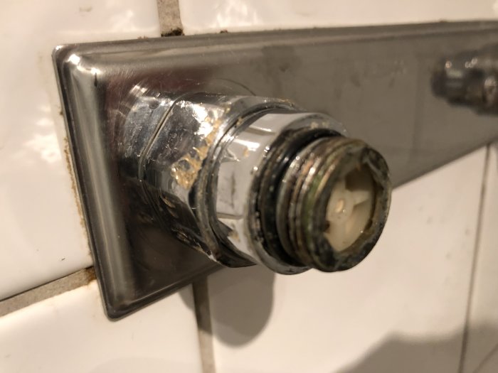 Demontage av en gammal kran med synlig rördel och mutter mot kakelvägg, tecken på vattenläckage och korrosion.