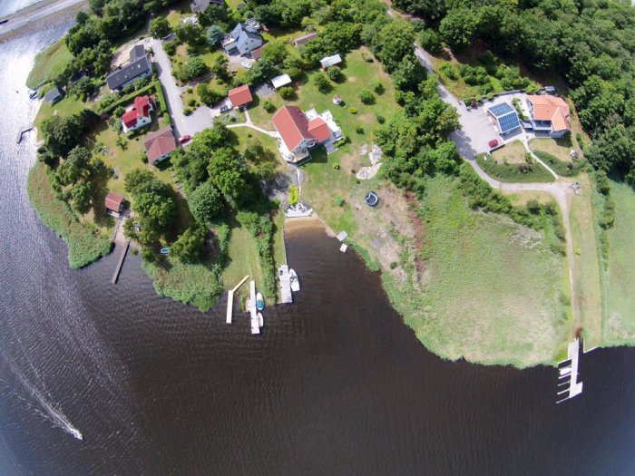 Flygbild av ett bostadsområde vid vatten med hus och båtbryggor, troligtvis för att visa husets läge.