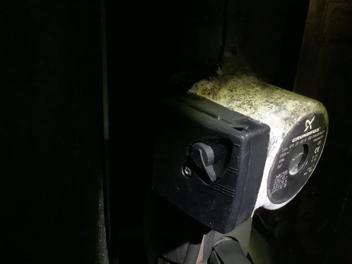 En vattenpump från Grundfos med inställningsvredet på läge 3, täckt med damm och belyst från sidan i ett mörkt utrymme.
