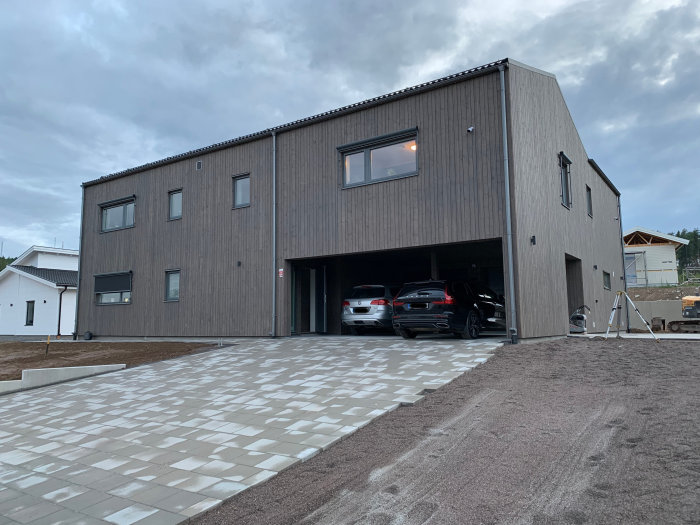 Nybyggt modernt hus med carport, integrerat garage och stenlagd uppfart.