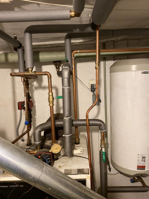 Värmepanna med anslutna rör och en varmvattenberedare i ett pannrum, söker hjälp för att återställa varmvatten.