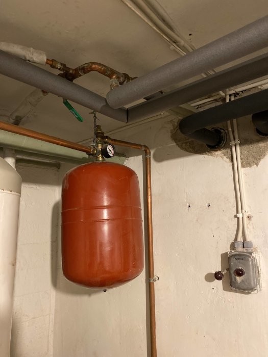 En värmepanna med anslutna rör och en grå expansionskärl installerat i en källare.