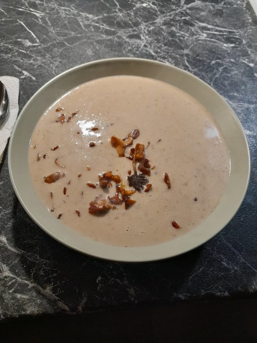 En tallrik med krämig svampsoppa toppad med stekta, egenplockade kantareller på ett marmorbord.