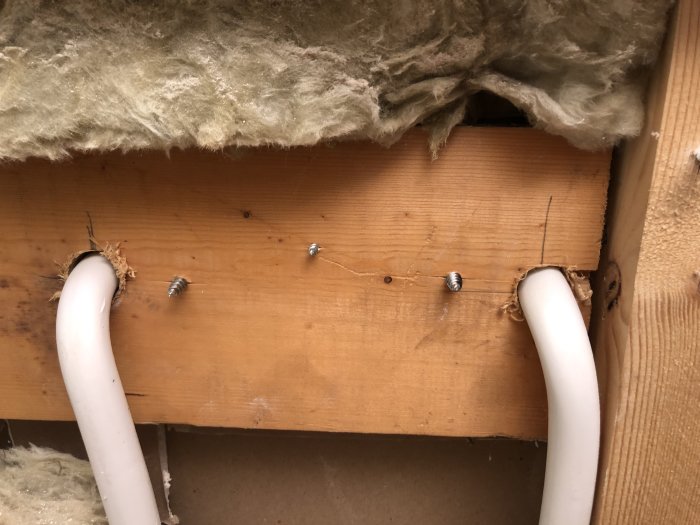 Två vita prisolrör som går genom en trävägg med isolering ovanför.