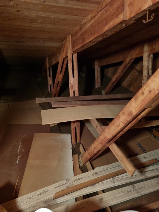 Oinredd vind med synliga takstolar, hanbjälkar och staplar av plyfa och annat brädmaterial på golvet.
