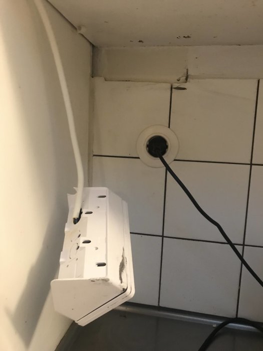 Ett lossnat eluttag med för små skruvar i hörnet mellan skåp och vit kakelvägg.