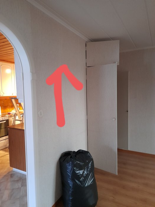 Interiör med en öppen dörr, markerad pil visar riktning för att ta bort skåpsida, kök i bakgrunden.