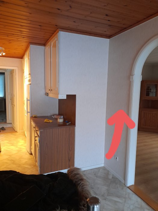 Kökshörna med skåp och frys intill en vit vägg med en pil som pekar på möjlig renovering.