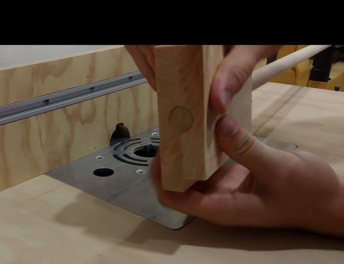 Hand håller ett träblock med fräst spår för att passa en rundstång, intill en arbetsbänk med fräsverktyg.