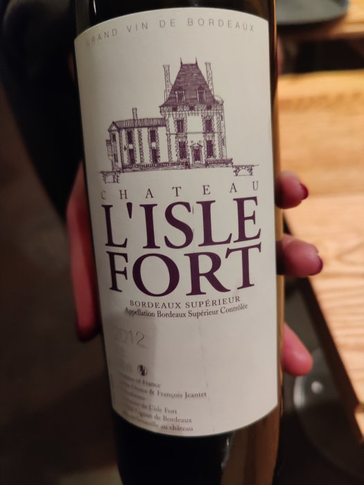 Hand håller en flaska vin märkt Chateau L'Isle Fort, Bordeaux Supérieur 2012.