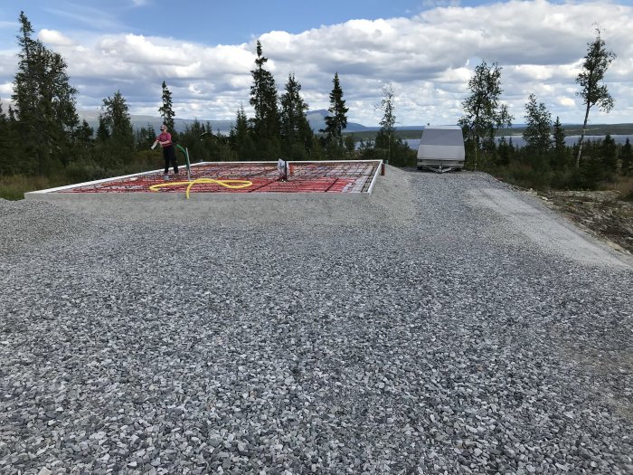 Person håller i en slang på en grund med markduk och spridd grus. Golvvärmeslang och kantelement installerade.