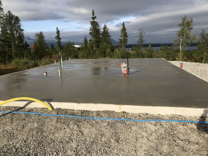 Nygräddad betongplatta med synlig armering och röranslutningar, omgiven av grus och randisolering.