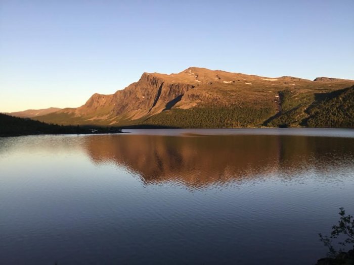 Utsikt över en sjö med berg i bakgrunden under solnedgång i Vojmådalen.