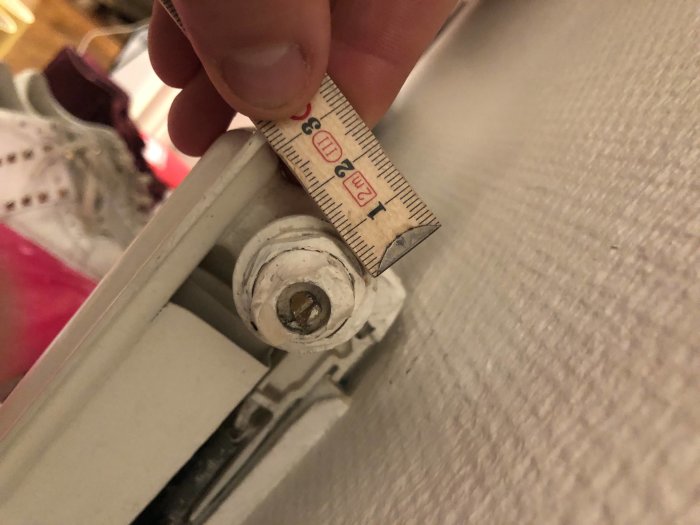 Hand mäter en trasig luftningsventil på ett radiatorselement med en tumstock.