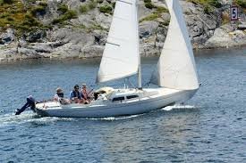 Segelbåt med personer ombord nära klippig kust.