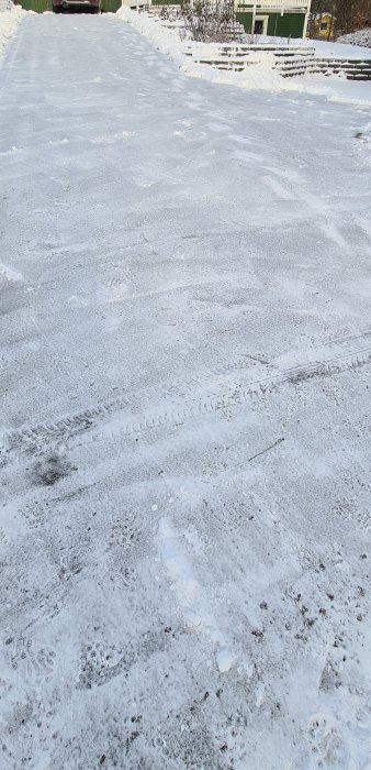 Isig och snöbelagd uppfart med fotspår och bilspår, omgiven av snötäckta trädgårdar.